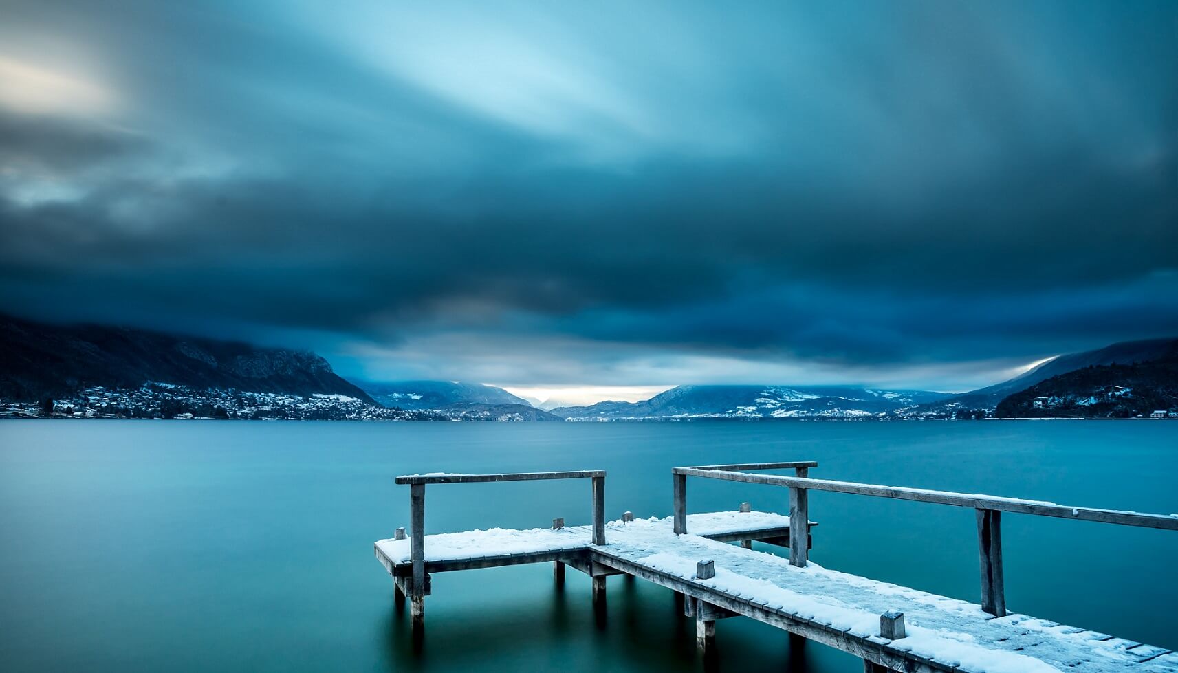 Vue du lac d'Annecy, hiver, ponton couvert de neige et nuages bas sur les montagnes