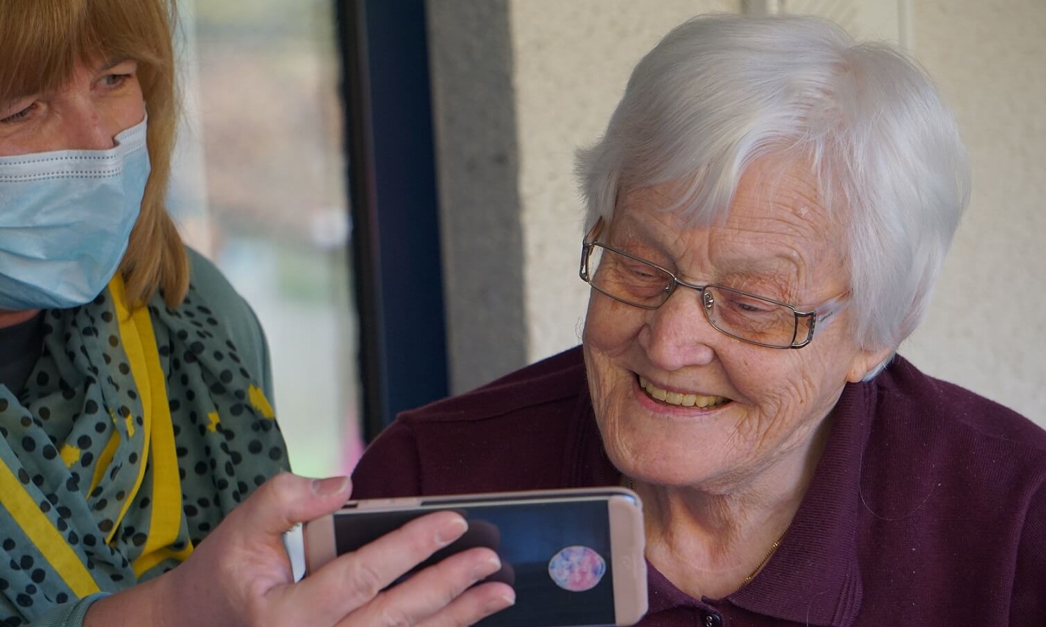 Aide soignante qui montre un téléphone à une personne âgée souriante