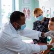 Homme avec blouse et masque, vaccine un enfant dans le bras, cabinet médical