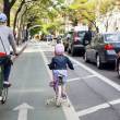 Femme et petite fille avec casques, de dos sur des vélos, voie cyclable en ville