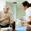 Homme âgé qui serre sa poitrine, parle avec une infirmière, décor de maison