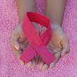 Symbol du ruban contre le cancer posé sur des mains avec un fond rose