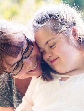 partenaire-social-solidaire - Femme adulte avec lunettes, appuie son visage contre l'épaule d'une jeune fille handicapée