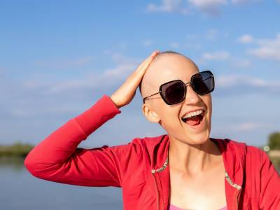 Femme chauve, sourit avec lunettes de soleil, bord de mer