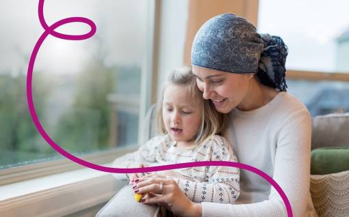 Femme avec un turban dans les cheveux, sourit avec sa fille sur les genoux.