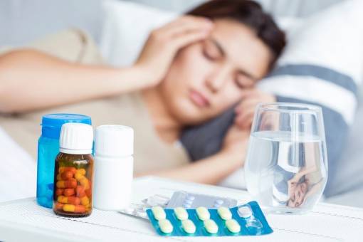 Une femme malade est couchée dans son lit et il y a des médicaments sur sa table de chevet