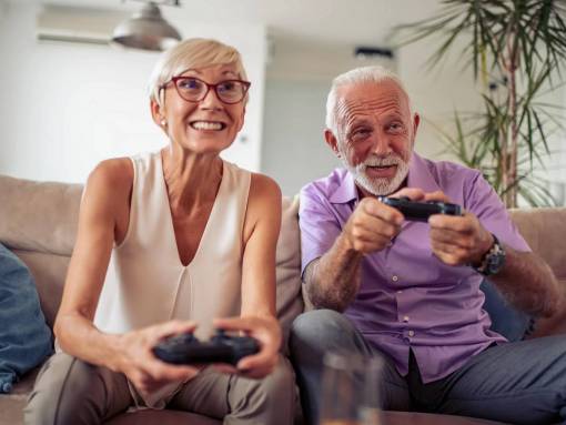Femme et homme avec cheveux blancs, jouent à la console vidéo sur un canapé