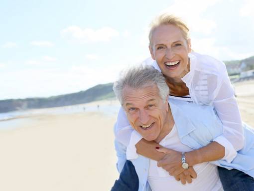 Femme senior, portée sur le dos de son compagnon aux cheveux gris, décor de plage