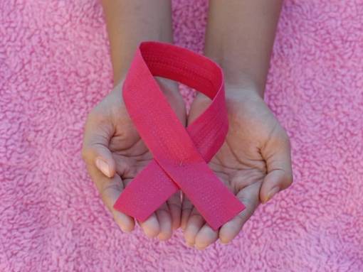 Symbol du ruban contre le cancer posé sur des mains avec un fond rose