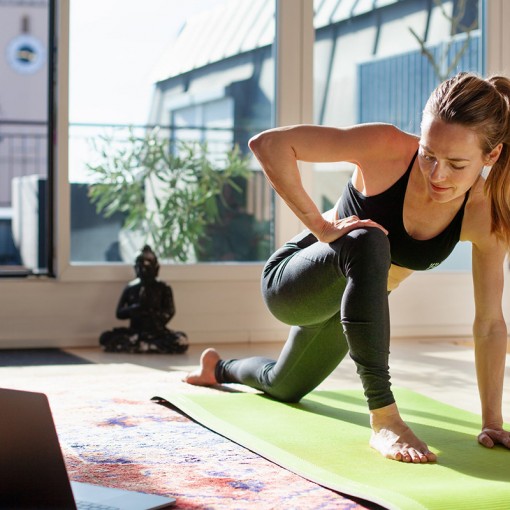 Femme qui fait des exercices d'assouplissement sur un balcon, tapis de yoga vert