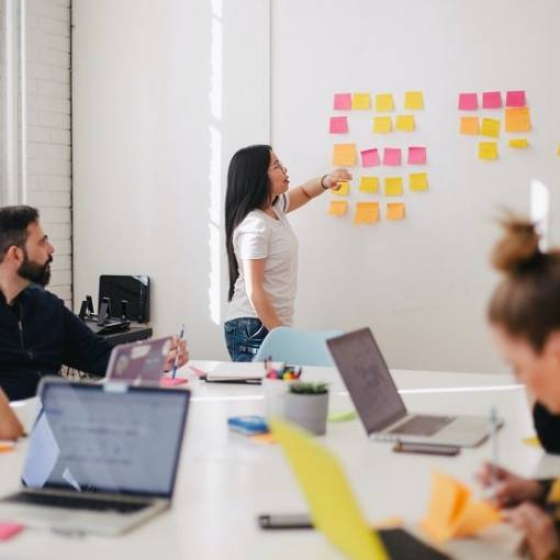 Réunion d'équipe au travail, avec plusieurs personnes autour d'une table et une femme au tableau