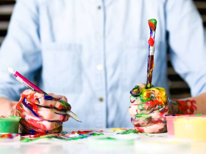 Mains d'adulte couvertes de peinture de couleur, tiennent un crayon et un pinceau