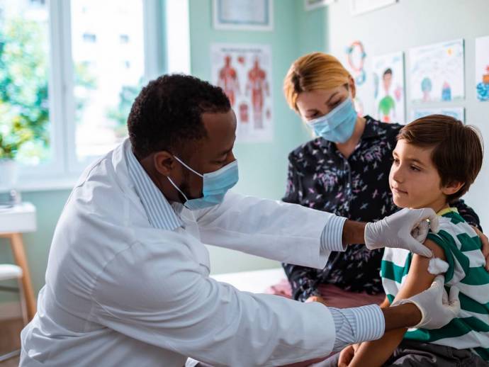 Homme avec blouse et masque, vaccine un enfant dans le bras, cabinet médical