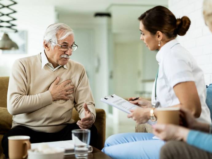 Homme âgé qui serre sa poitrine, parle avec une infirmière, décor de maison