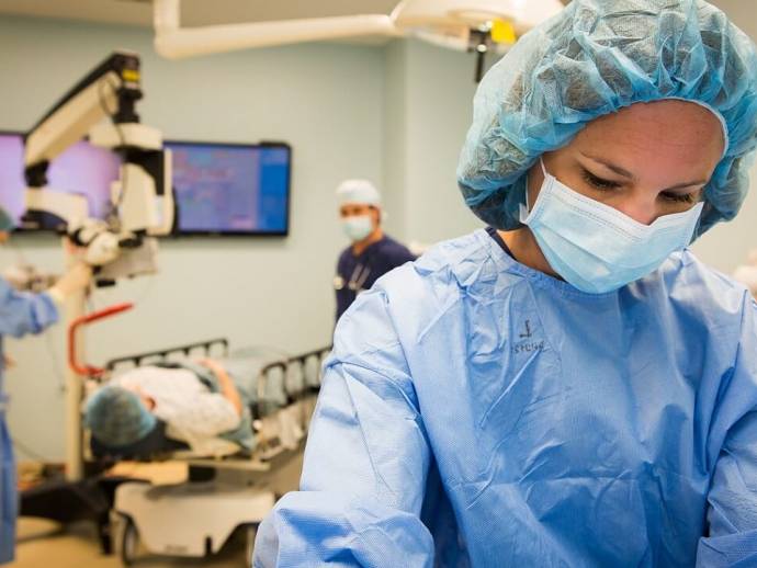 Femme en tenue de bloc d'hôpital bleu. En arrière plan, personne sur un lit