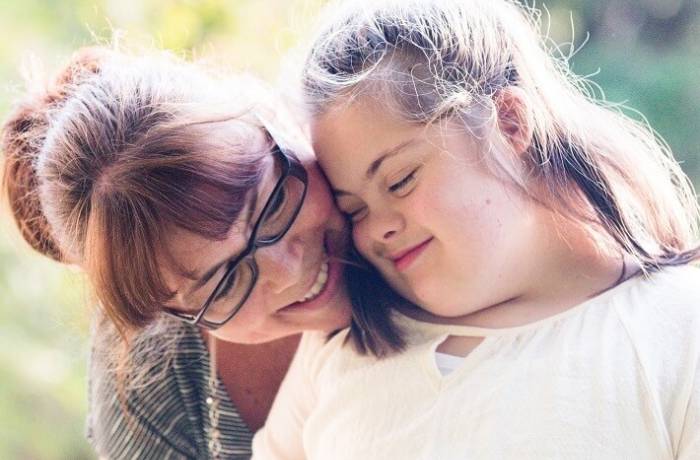 partenaire-social-solidaire - Femme adulte avec lunettes, appuie son visage contre l'épaule d'une jeune fille handicapée