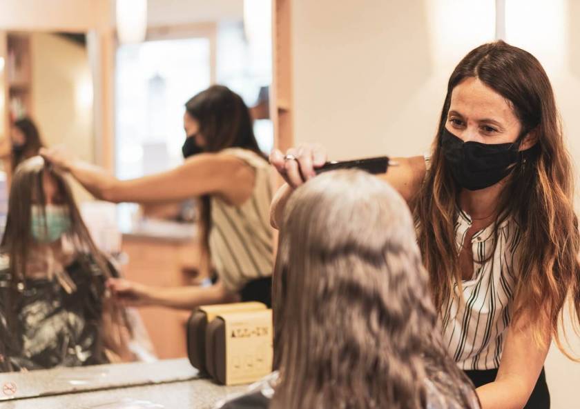 Femme coiffe une femme devant un miroir, avec masque noir