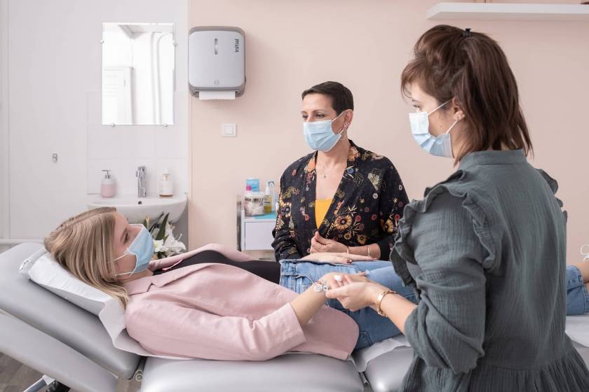 Marion, socio-esthéticienne, et une maman, massent les mains d'une patiente