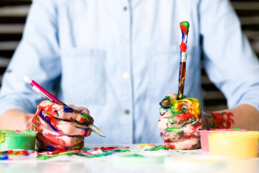 Mains d'adulte couvertes de peinture de couleur, tiennent un crayon et un pinceau
