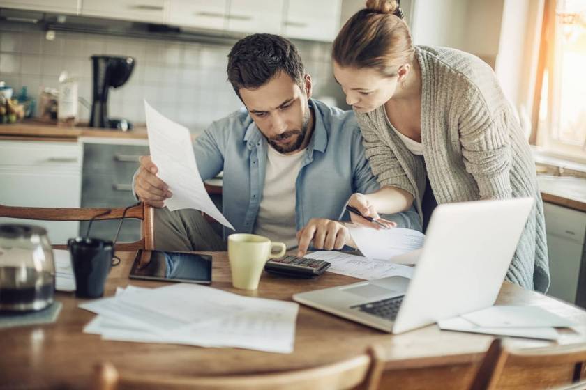 Homme et femme penchés sur une calculatrice, avec des papiers, l'air soucieux