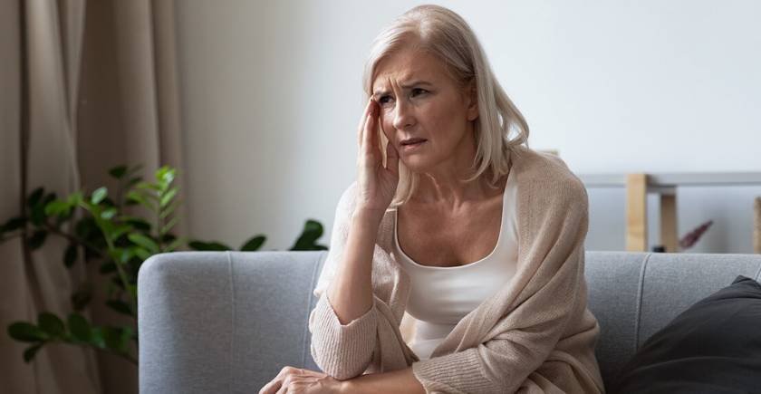 Femme senior, assise sur un canapé, main à la tête comme avec une migraine