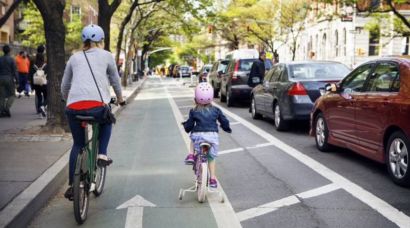 Femme et petite fille avec casques, de dos sur des vélos, voie cyclable en ville