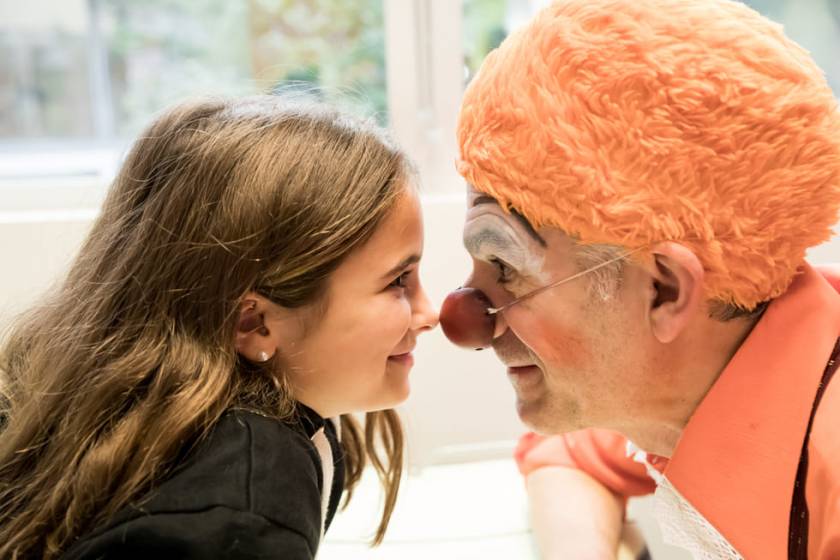 Clown Panoli, perruque orange, nez rouge appuyé contre le nez d'une petite fille