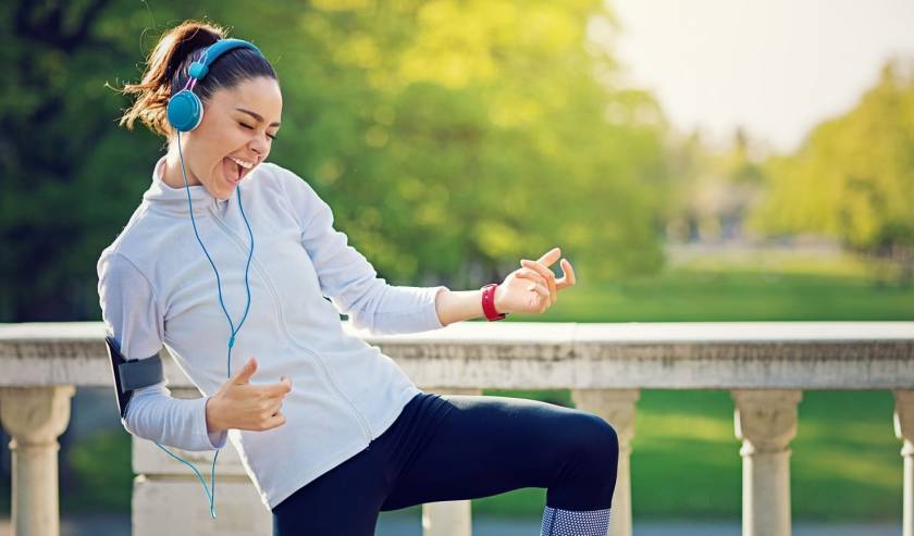 Jeune femme en tenue de sport, casque audio sur les oreilles dans un parc. Joue de la air guitar