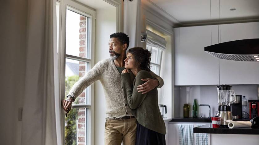 Homme et femme enlacés dans une cuisine, regardent par la fenêtre