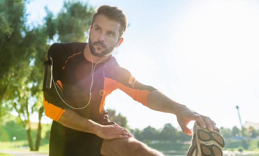 Homme avec casque de musique, s'étire les jambes, tenue de course