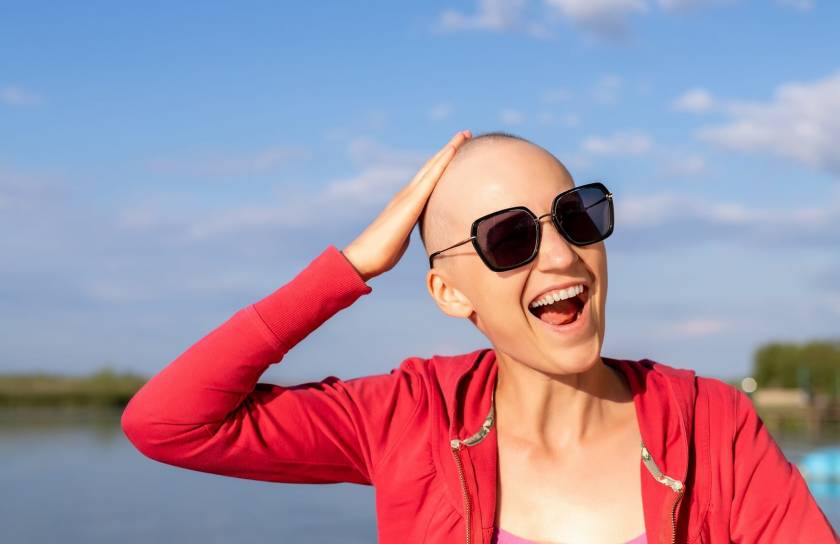 Femme chauve, sourit avec lunettes de soleil, bord de mer