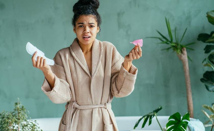 Jeune femme en peignoir, avec serviette hygiénique et cup à la main, dans sa salle de bains