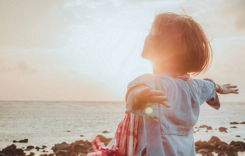 Femme qui étend les bras, regarde le soleil couchant