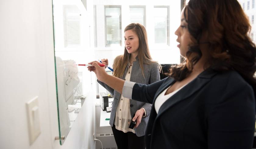 2 femmes écrivent sur un tableau blanc, vue de profil