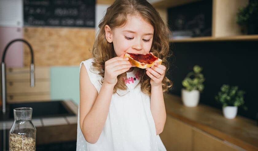 Petite fille qui croque une tartine de pain et confiture