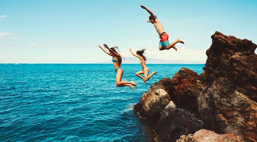 3 personnes en maillot sautent d'une falaise dans l'eau