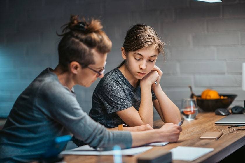 Une femme donne du soutien scolaire à un adolescent sur une table