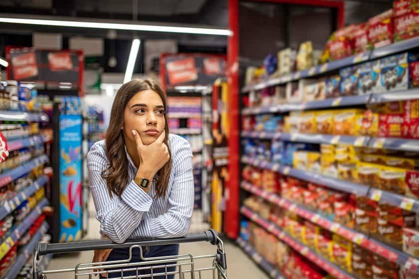Une femme avec son cadi réfléchit devant un rayon de supermarché