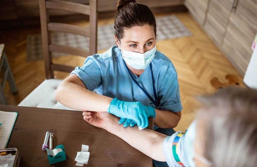 Une médecin fait une prise de sang à un patient à son domicile