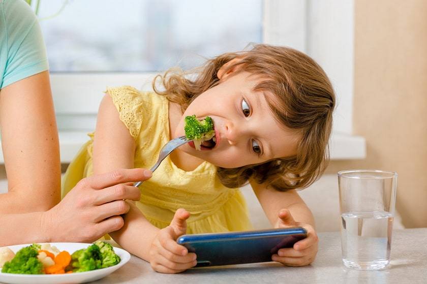 Petite fille qui mange devant un téléphone