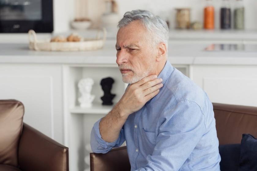 Un senior est chez lui et se touche la gorge près de la thyroïde