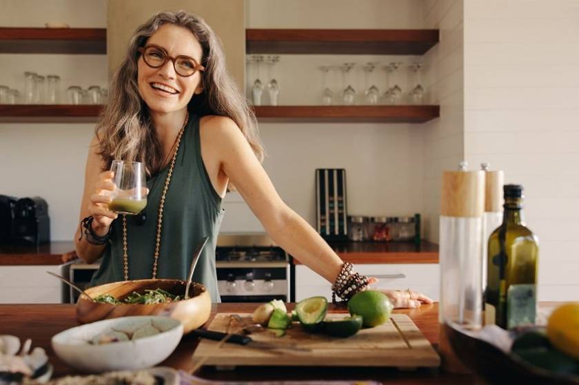 Une femme dans sa cuisiner boit un jus aux légumes