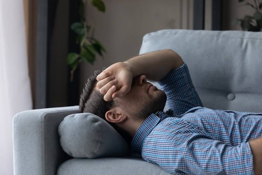 Un homme avec une migraine est couché sur un canapé et a son bras posé sur le front