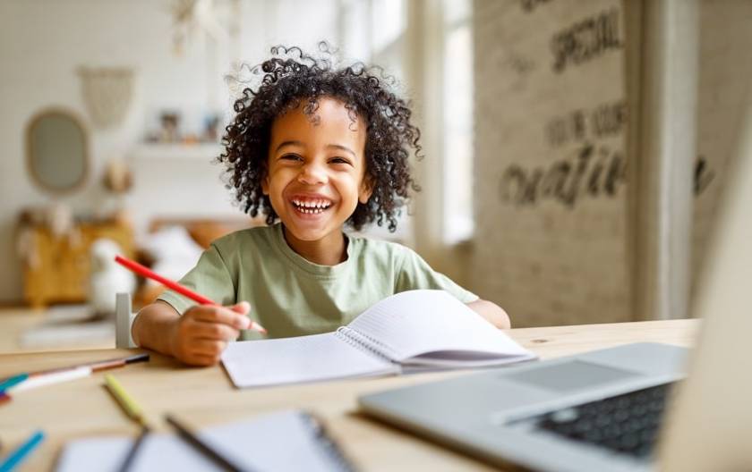 Une petite fille souriante est assise en face d'un bureau chez elle