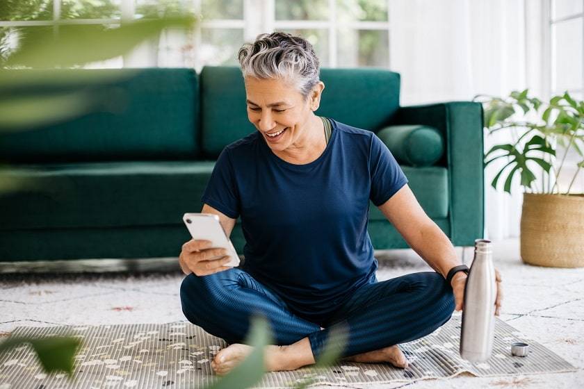 Femme assise confortablement dans on salon souriant en regardant son téléphone