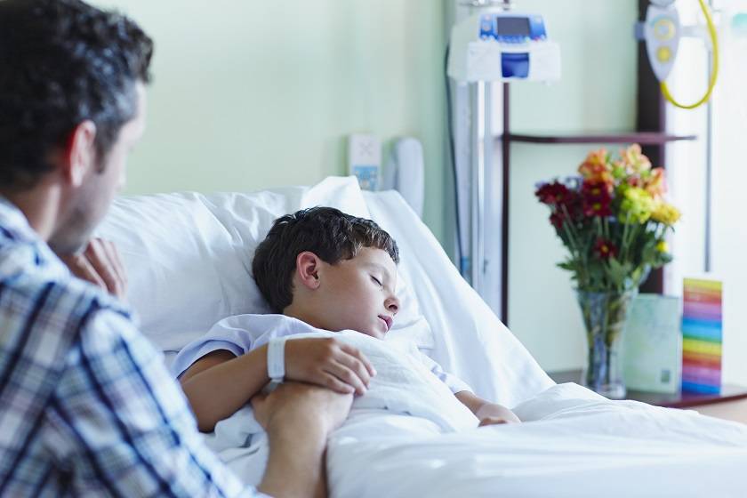 Petit garçon allongé dans un lit d'hôpital accompagné de son père lui tenant la main