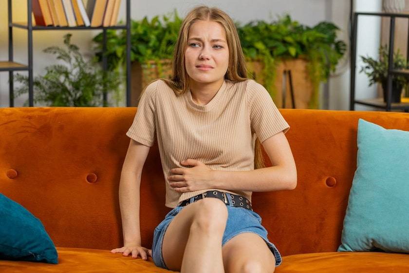 Femme assise sur un canapé se tenant le ventre